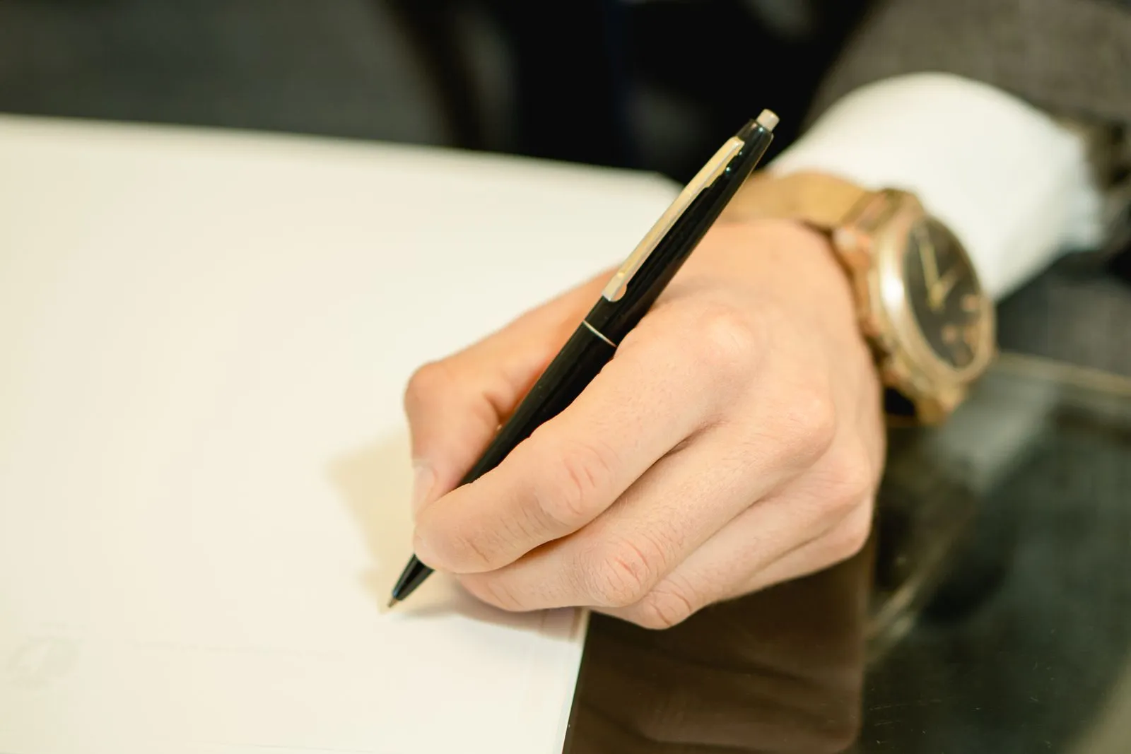 A close-up image of a hand holding a pen and writing on white paper, symbolizing business and communication.